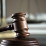 A wooden gavel and sound block in the foreground with scale and books out of focus in background