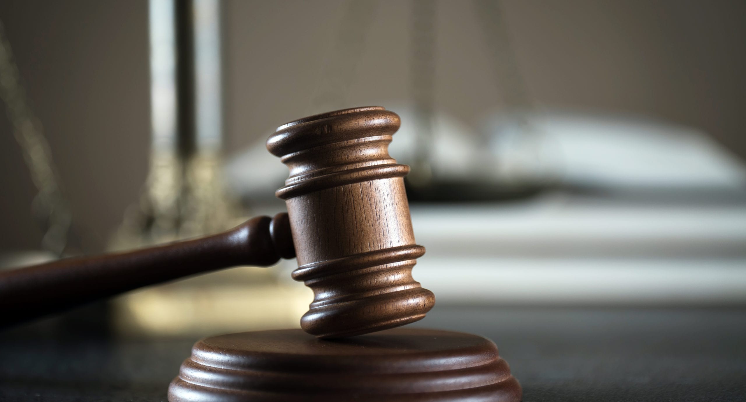 A wooden gavel and sound block in the foreground with scale and books out of focus in background