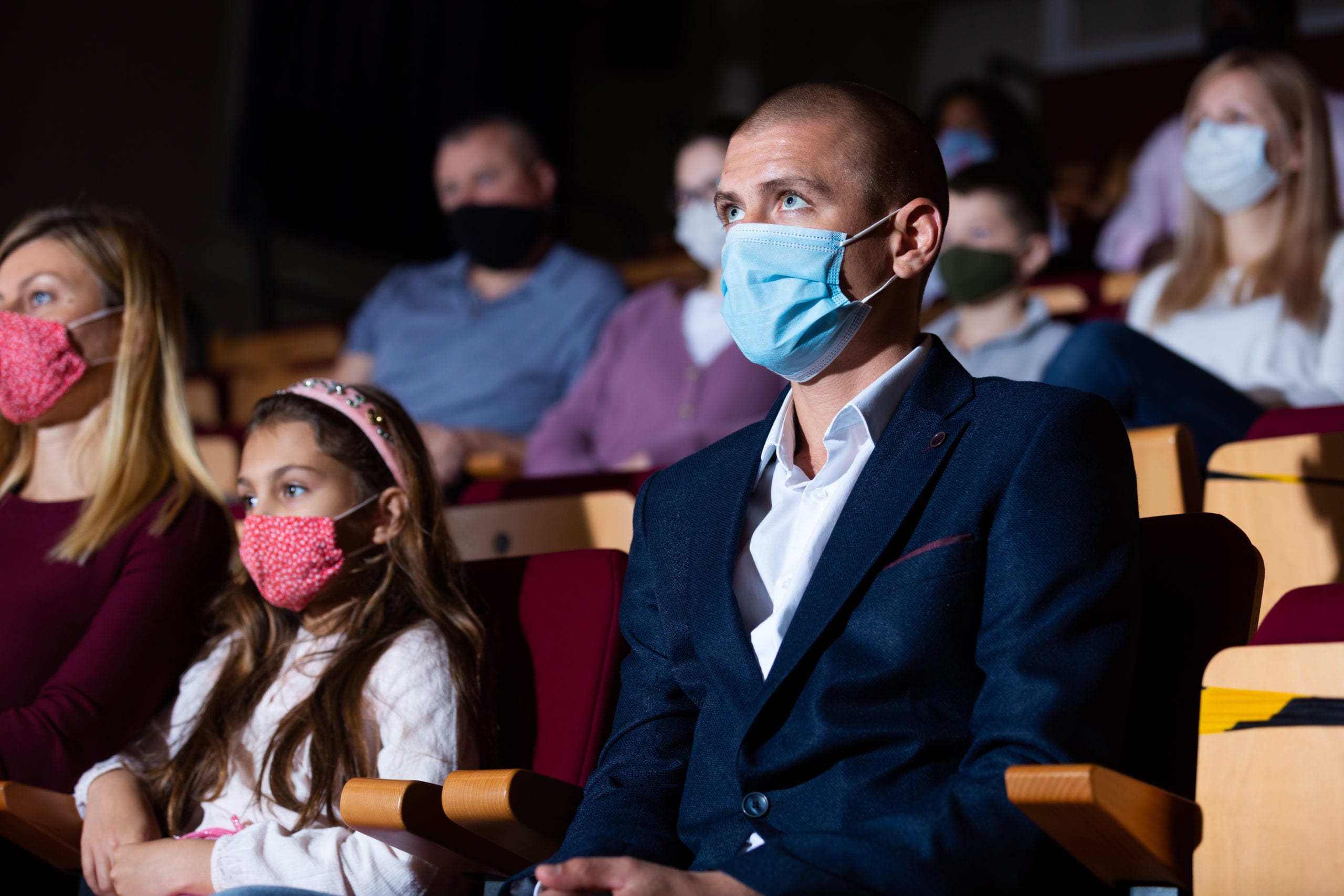 Adults and a child wearing face coverings while seated in a theater