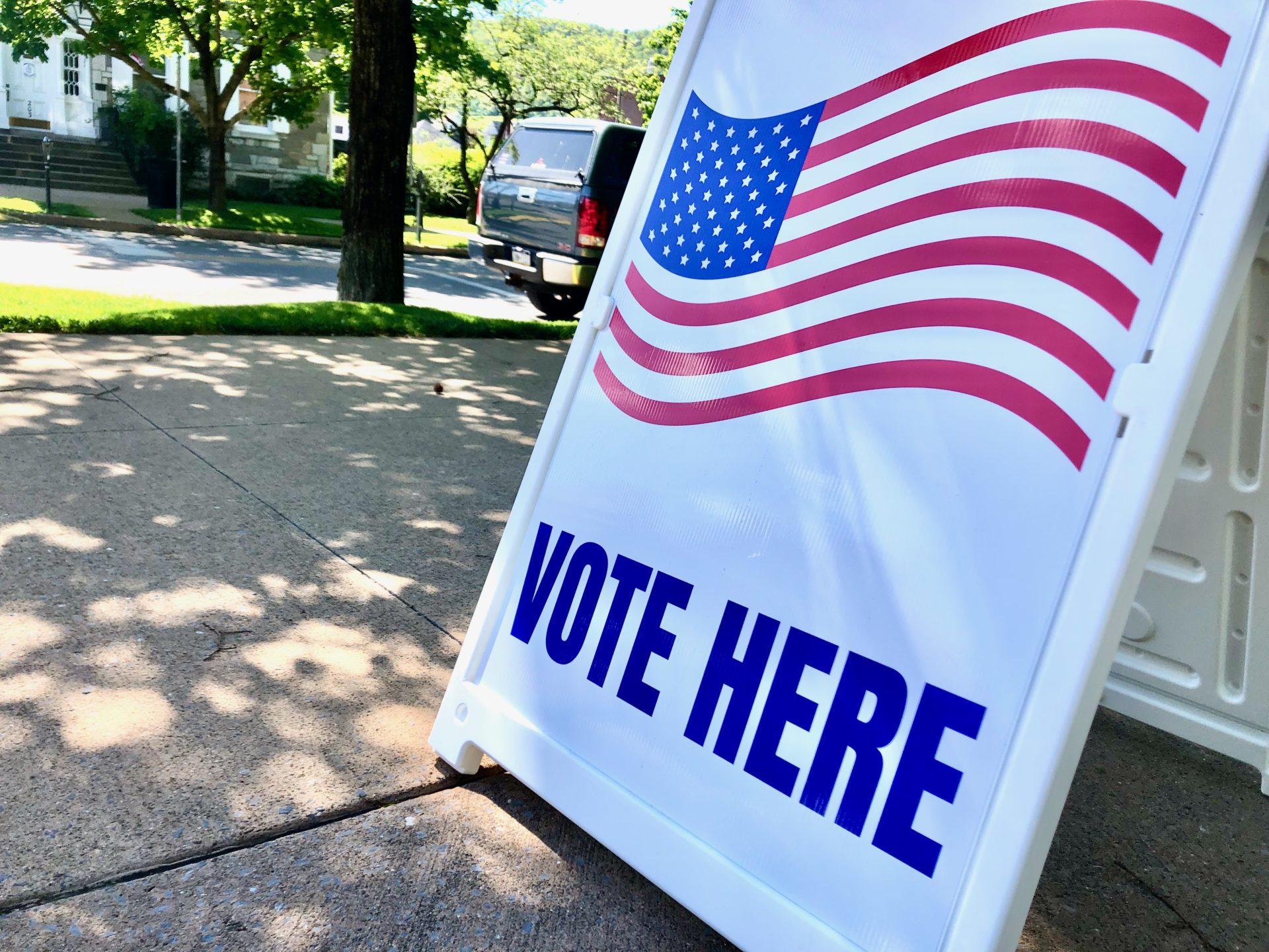 White sign with "Vote Here" in blue letters below the U.S. flag