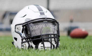 Penn State football helmet on grass with football in the background