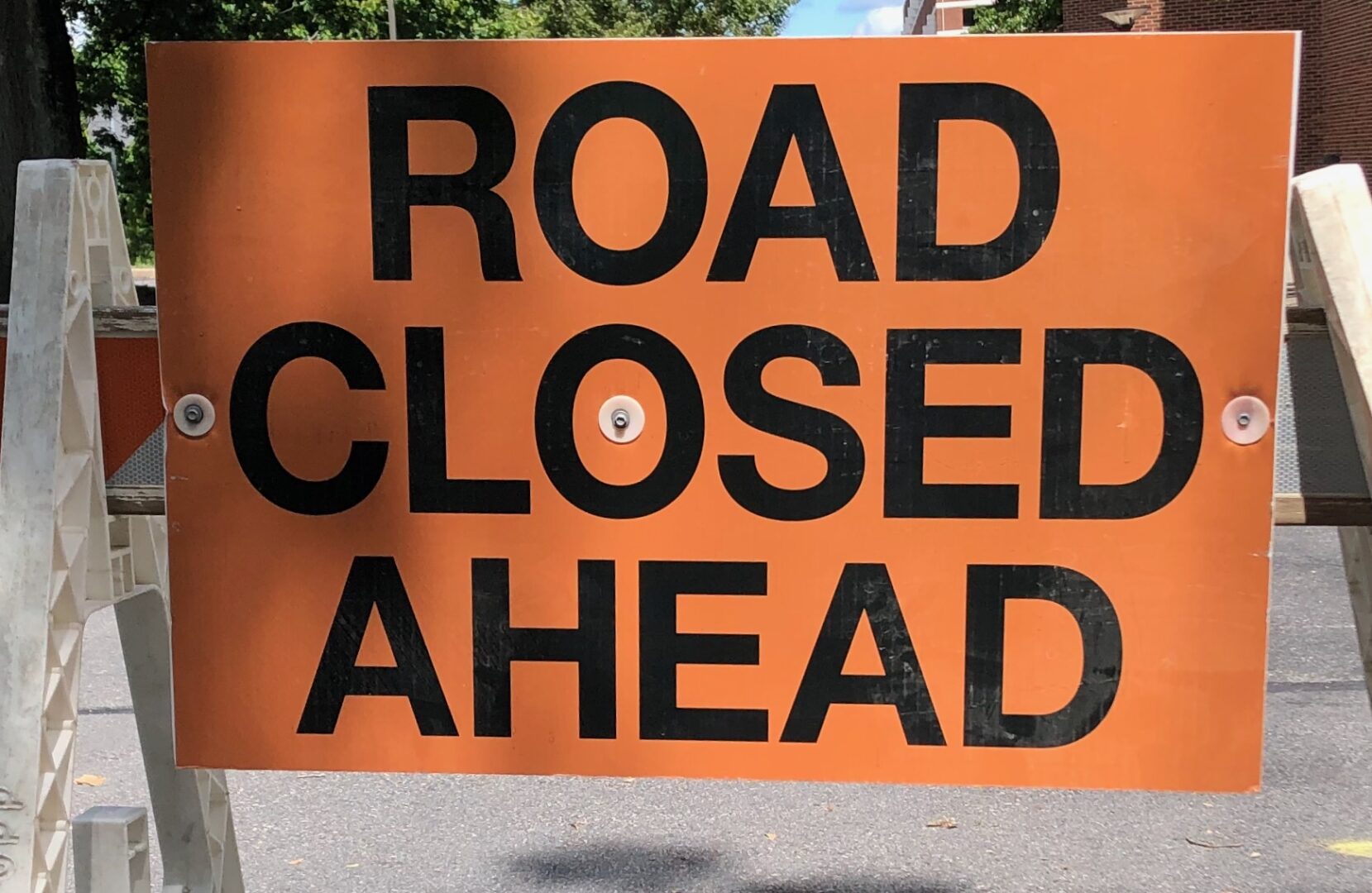Orange sign with black letters reading "Road Closed Ahead"