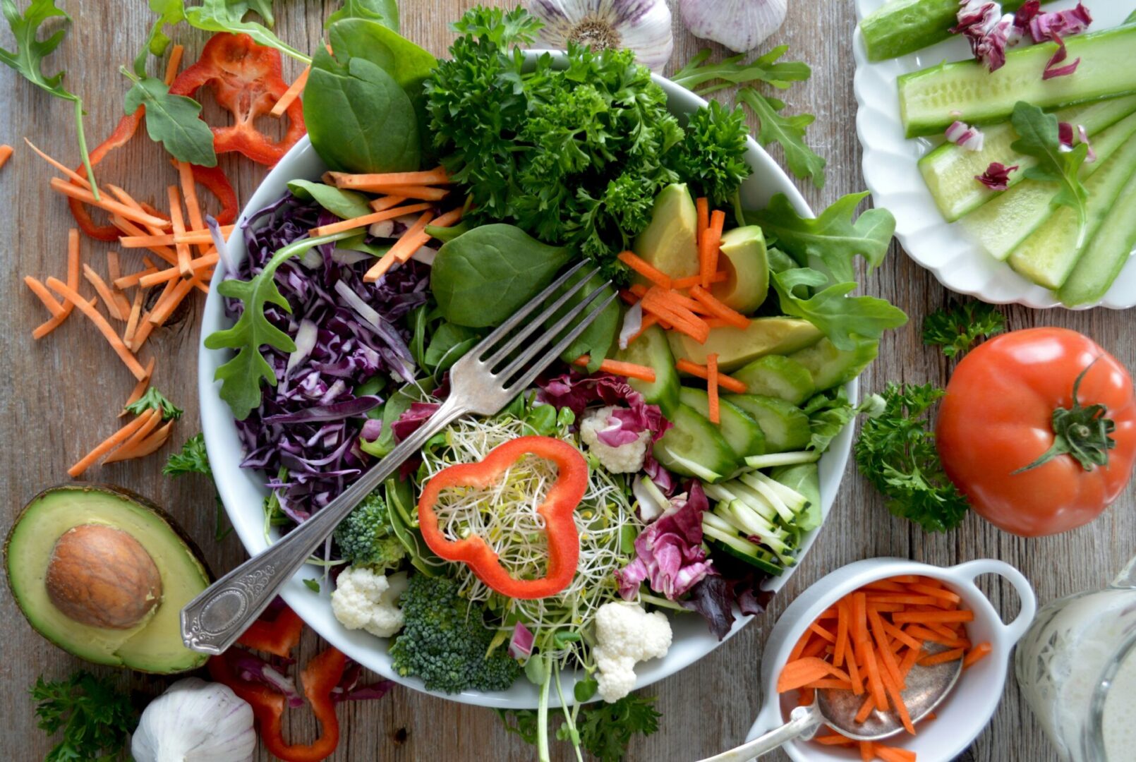 Spinach salad with peppers radish in a bowl surrounded by carrots tomatoes and avocados